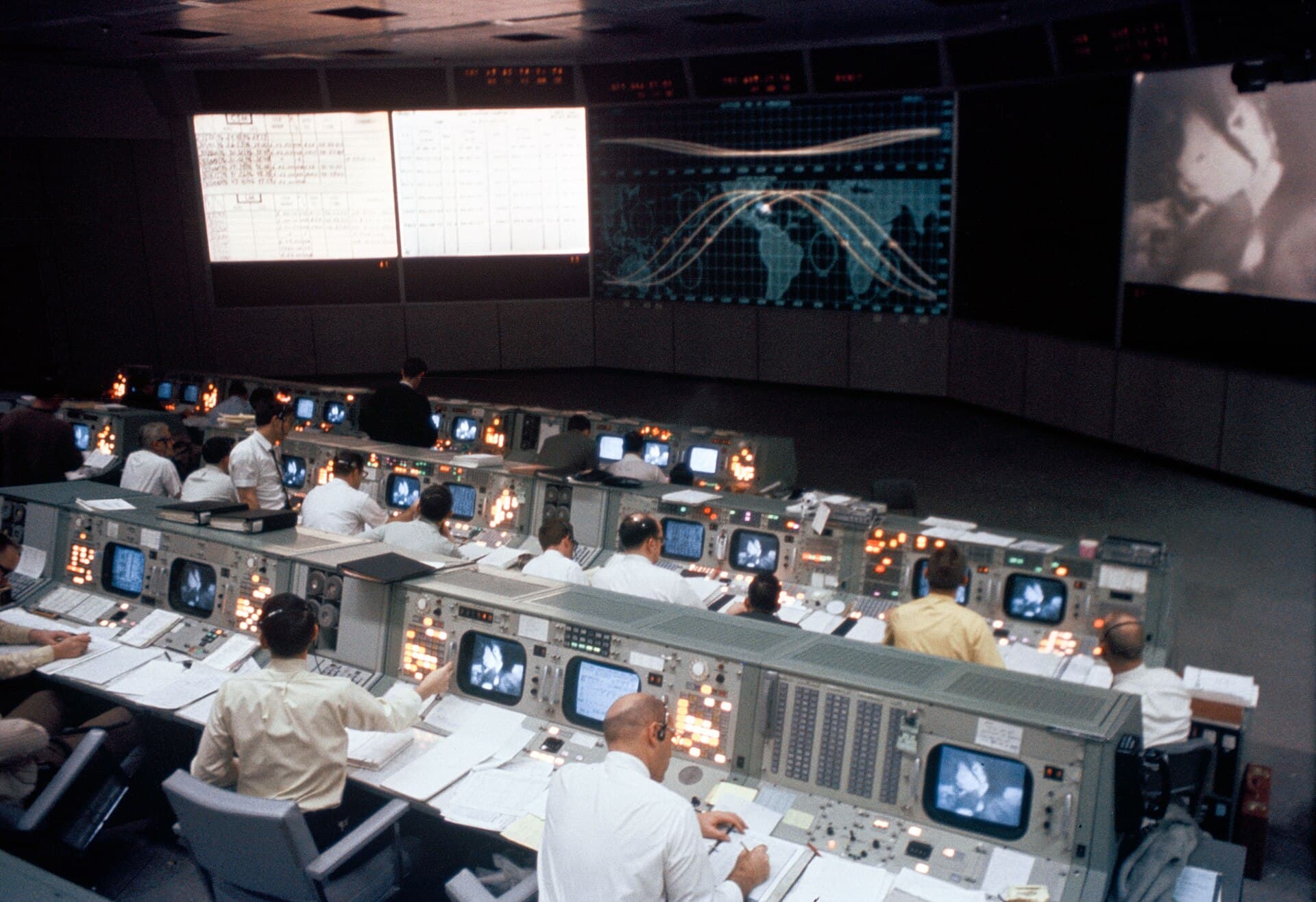 Flight controllers at rows of consoles in NASA's Mission Operations Control Room during Apollo 9, with wall-sized displays ahead